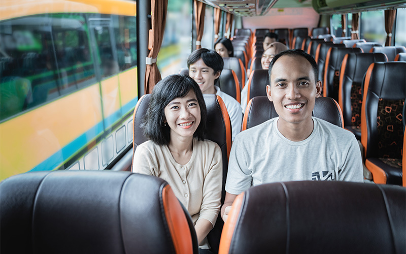 Passengers sit inside modern bus, two smiling at camera.
